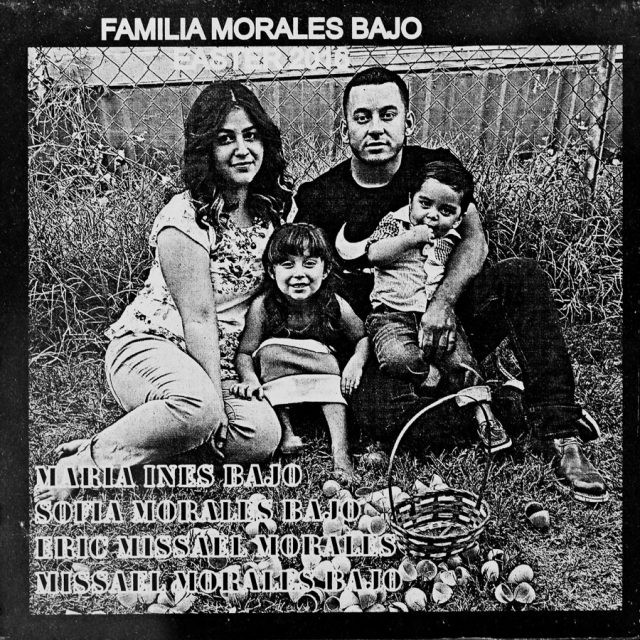 A mother and father sit on the grass with their two young children with an easter basket and pile of opened easter eggs in front of them engraved on marble panel at Maze of Honor