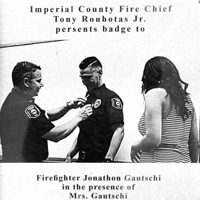 Engraving of a firefighter in uniform receiving a badge from the fire chief as a female looks on