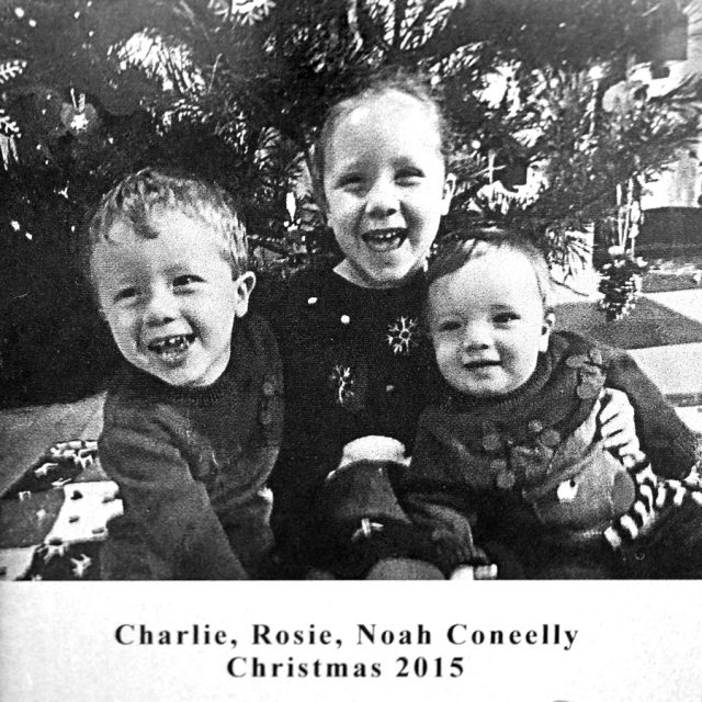 Engraving of three young children seated smiling in front of a Christmas tree on a panel at the Maze of Honor