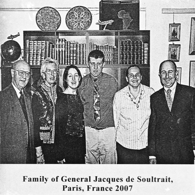 Smiling family members of General Jacques de Soultrait standing in front of a book case engraved on marble slab for Maze of Honor
