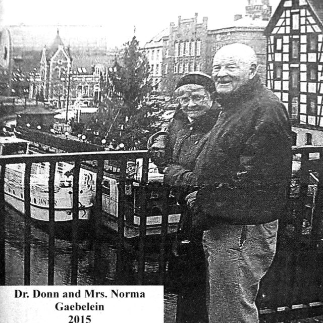 An elderly man and woman stand on bridge above a canal engraved on marble panel for Maze of Honor