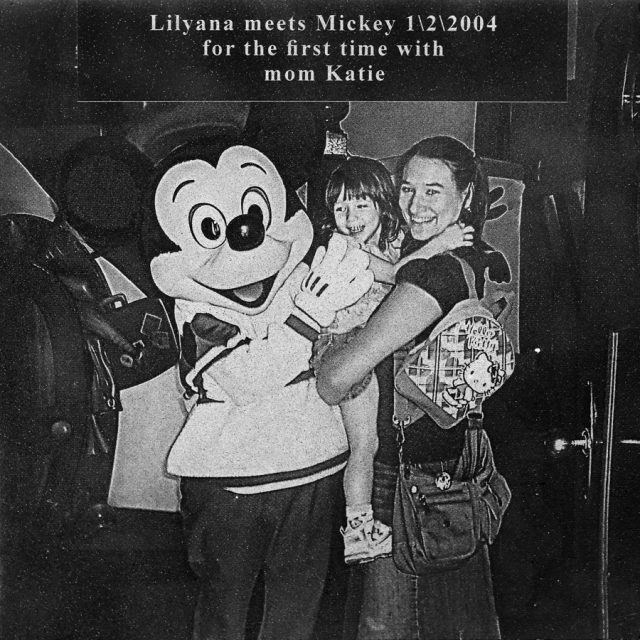 A mother holding her daughter stands next to Mickey Mouse engraved on marble panel at Maze of Honor