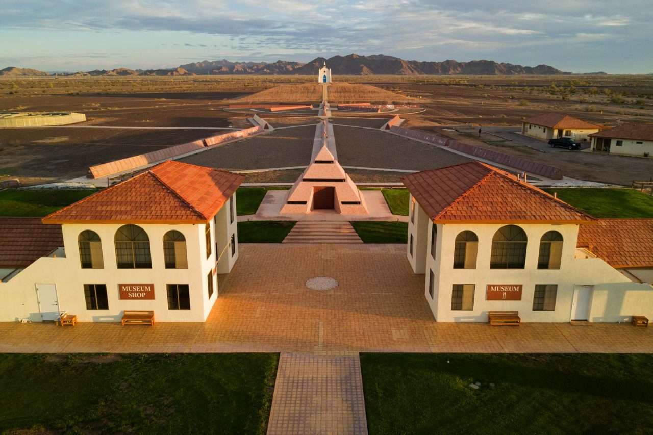 Aerial view of the History of Humanity in Granite monuments, Center of the World pyramid, Hill of Prayer, and Church on the Hill with California mountains in the background
