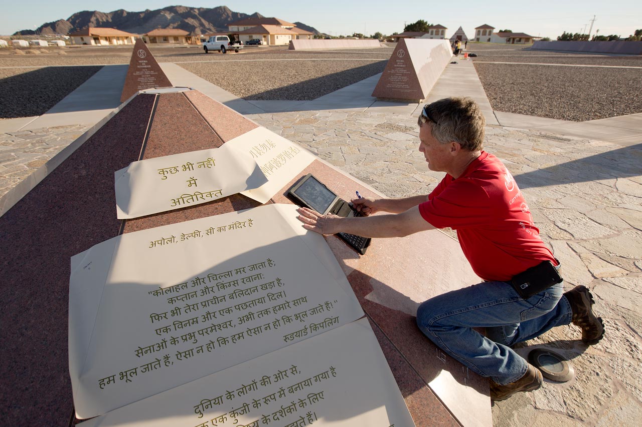 A man in a red shirt kneels next to the Felicity Stone with a smart tablet charting out the sizes of the inscriptions