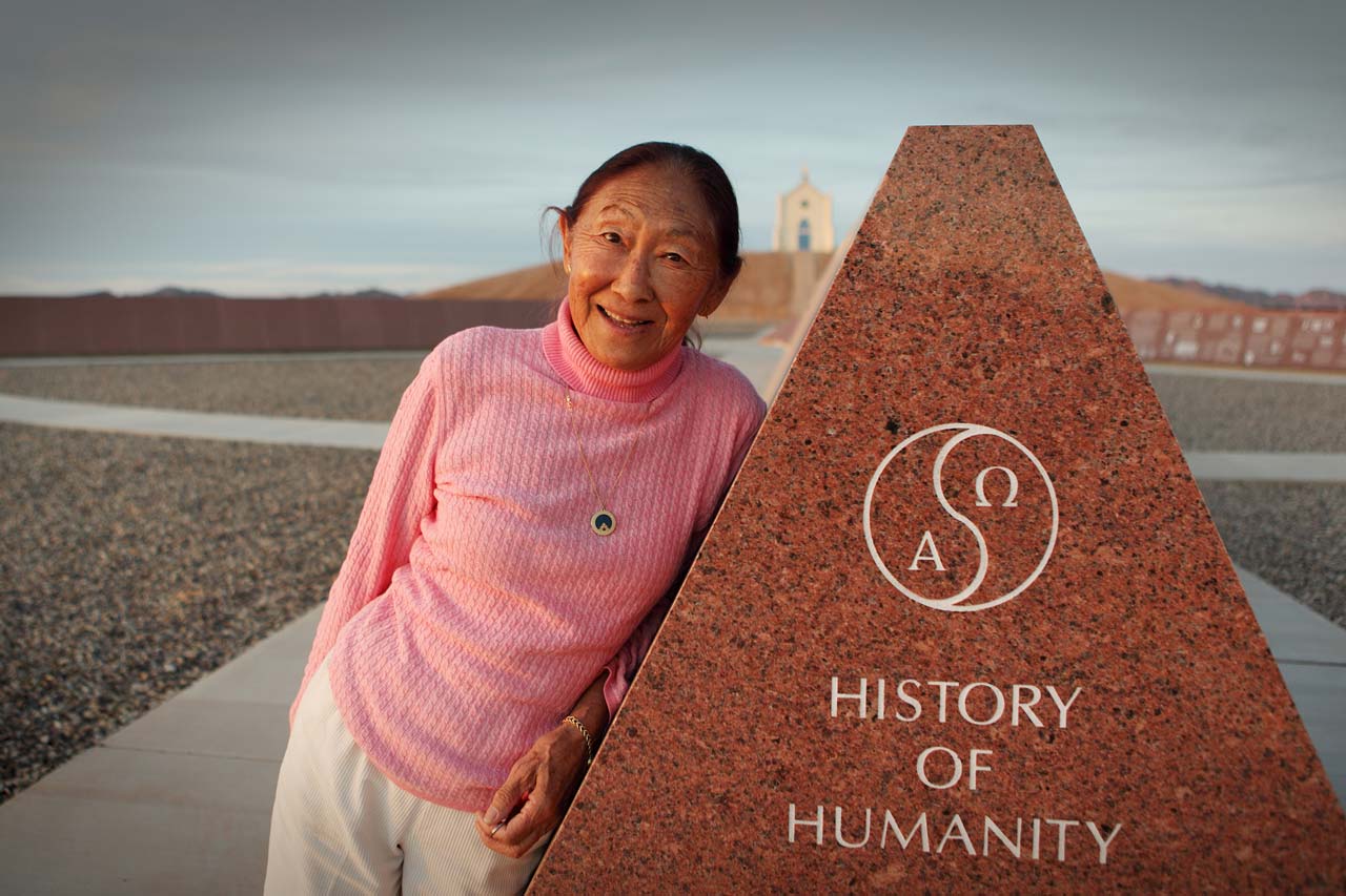 Felicia in a cable knit pink turtle neck leans against a Missouri Red granite monument at the History of Humanity in Granite