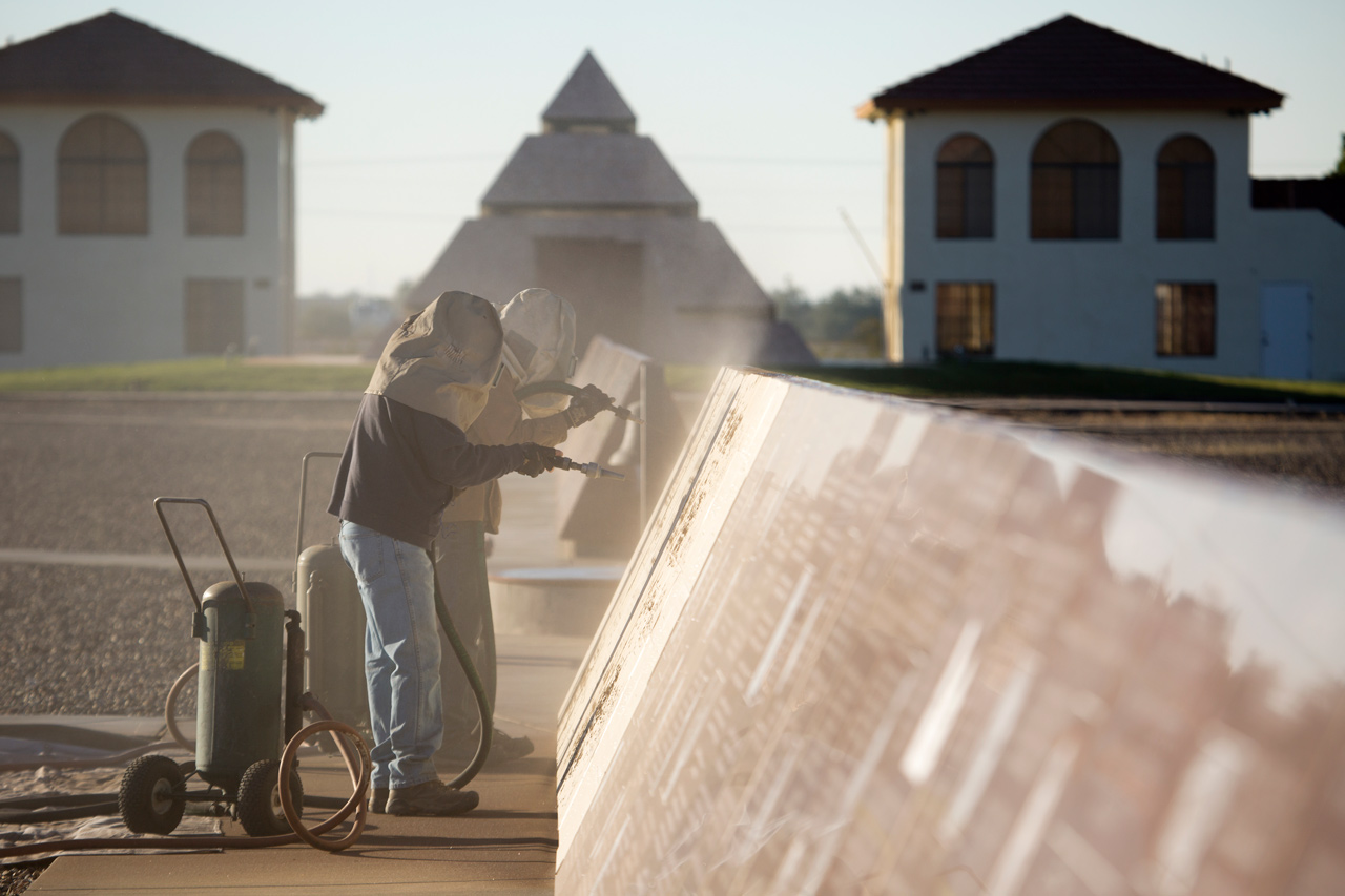 Two individuals in protective head gear use sandblasters to etch into a Missouri Red granite monument at the History of Humanity in Granite