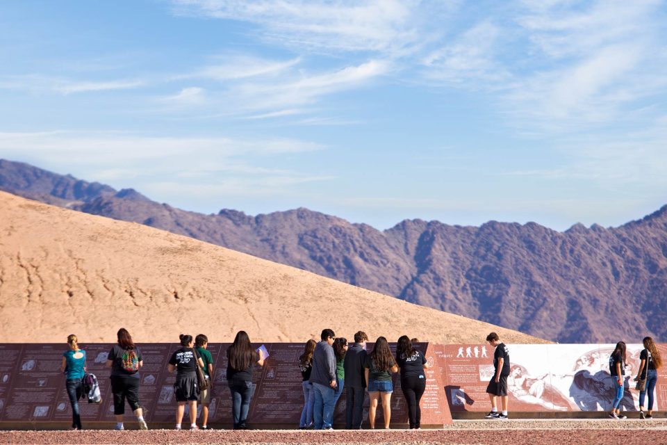 Group of young adults stand in front of granite panel at the museum of history in granite near Yuma, Arizona with mountain range in the background