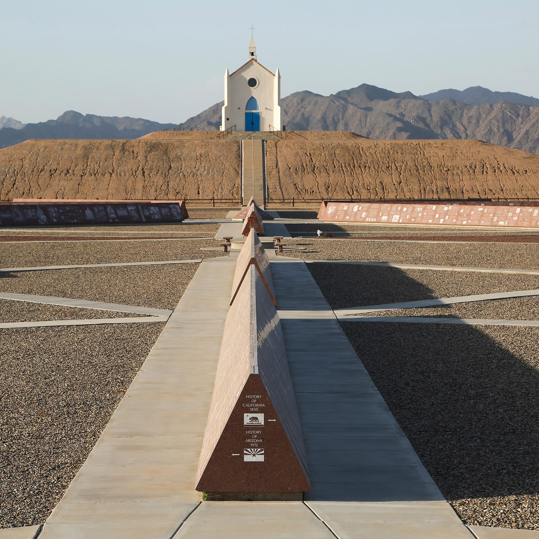 White church with blue doors and round stained glass window atop the hill of prayer behind the History of California exhibit at the History of Humanity in Granite