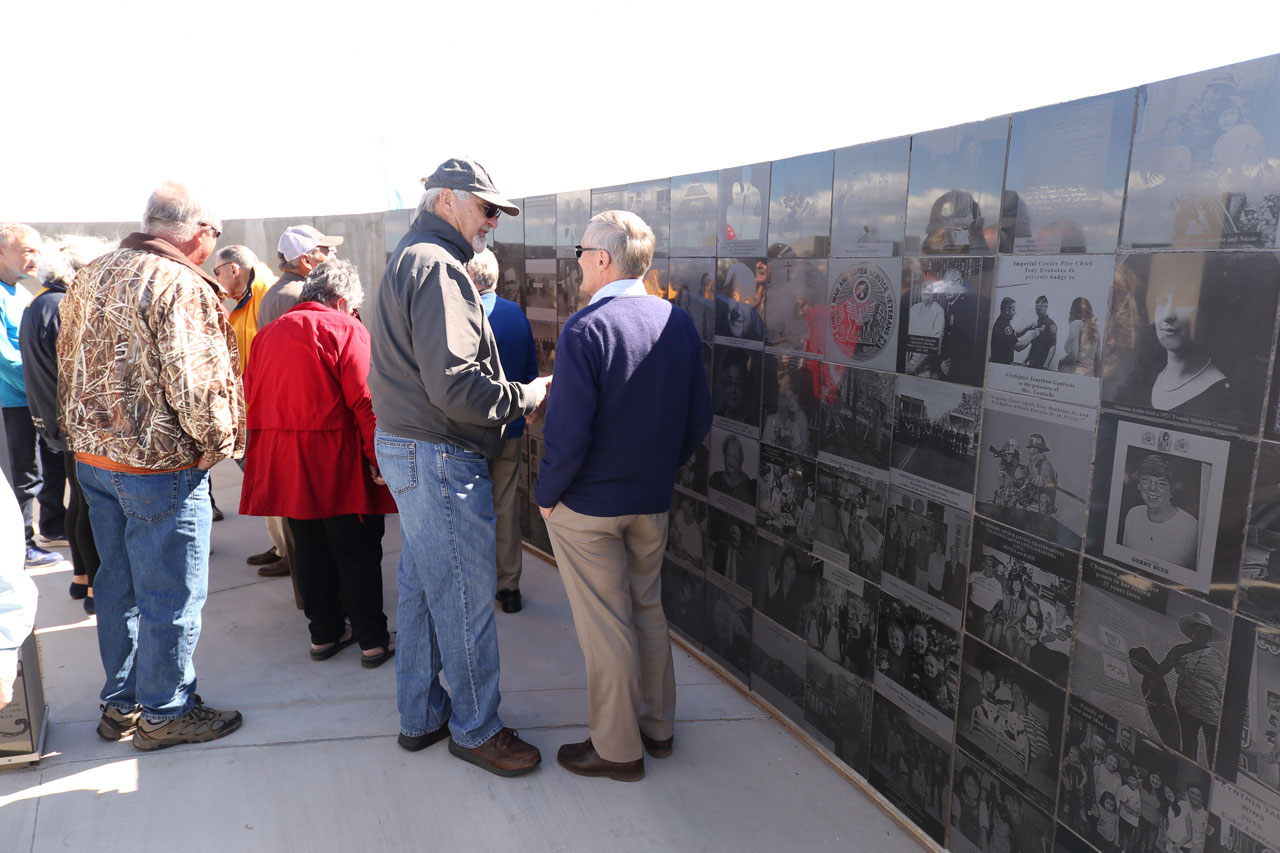 A crowd of older men and women stand in front of engraved marble panels lining the walls of the Maze of Honor