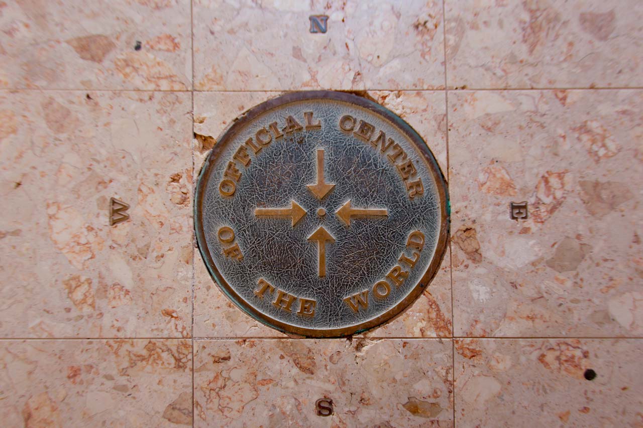 Metal plaque on a marble floor which reads Official Center of the World with the cardinal directions around it